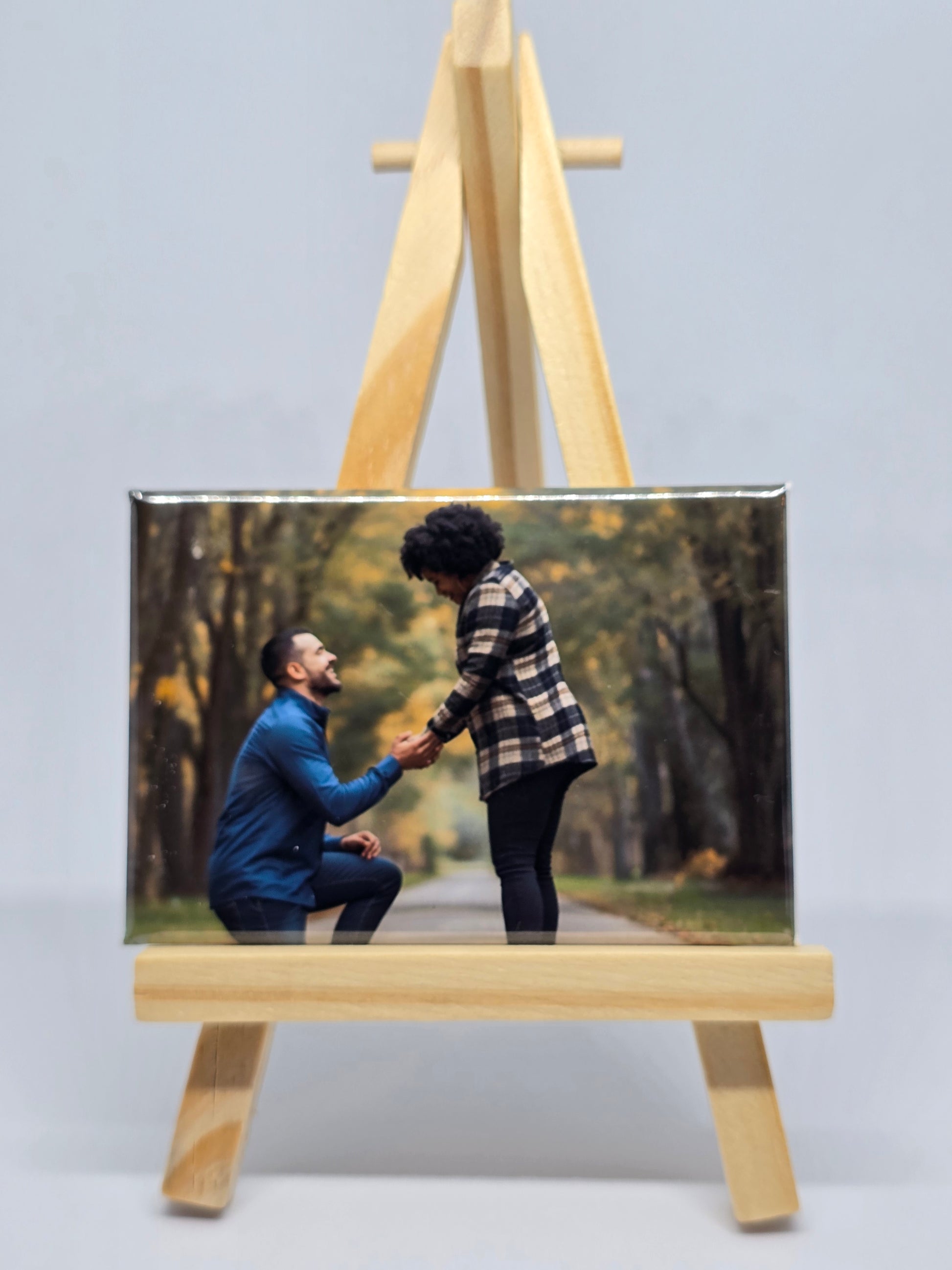Two people holding hands in a scenic outdoor setting displayed on a wooden stand.