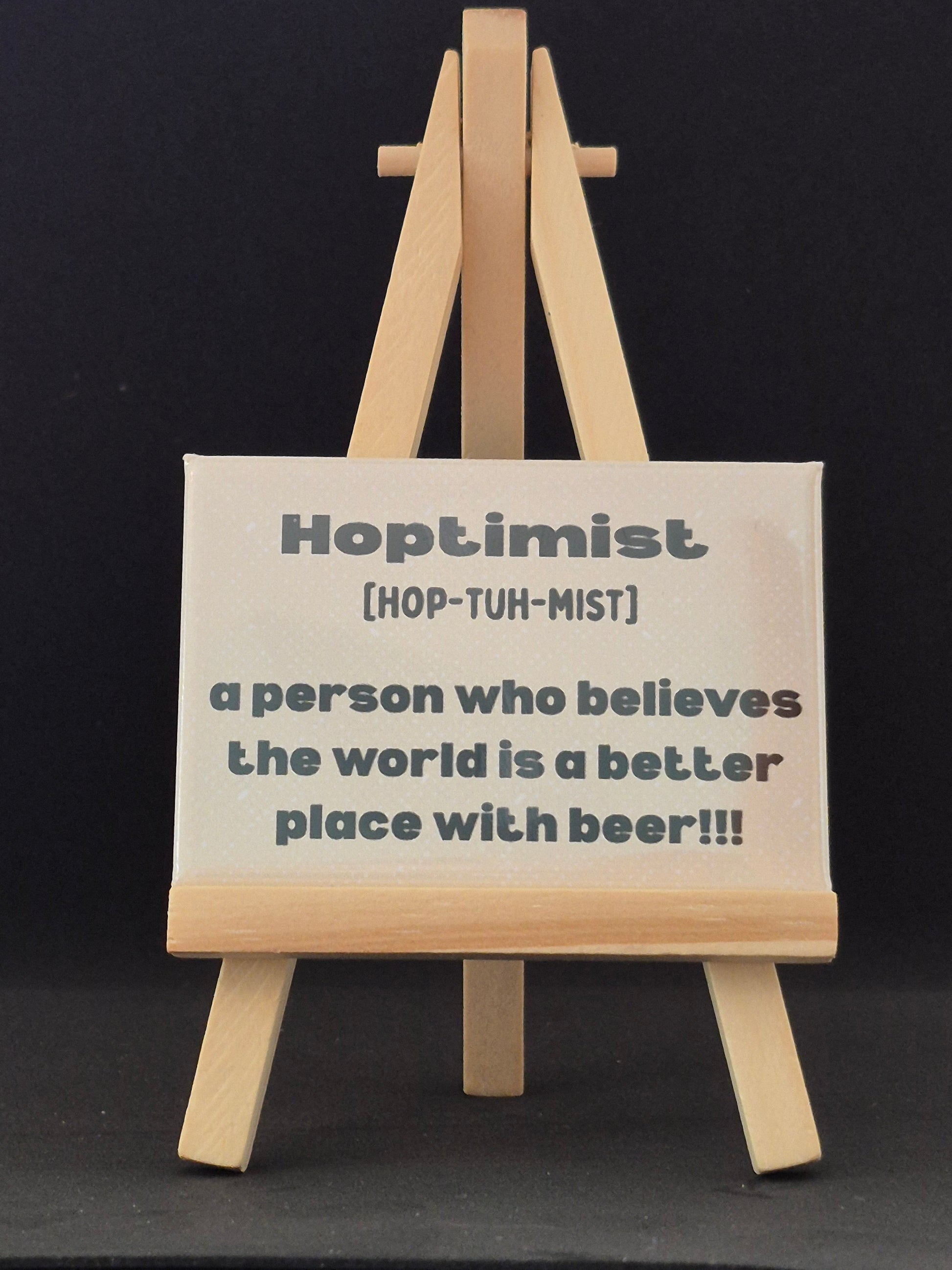 Wooden sign with definition of 'optimist' and humorous text on a black background